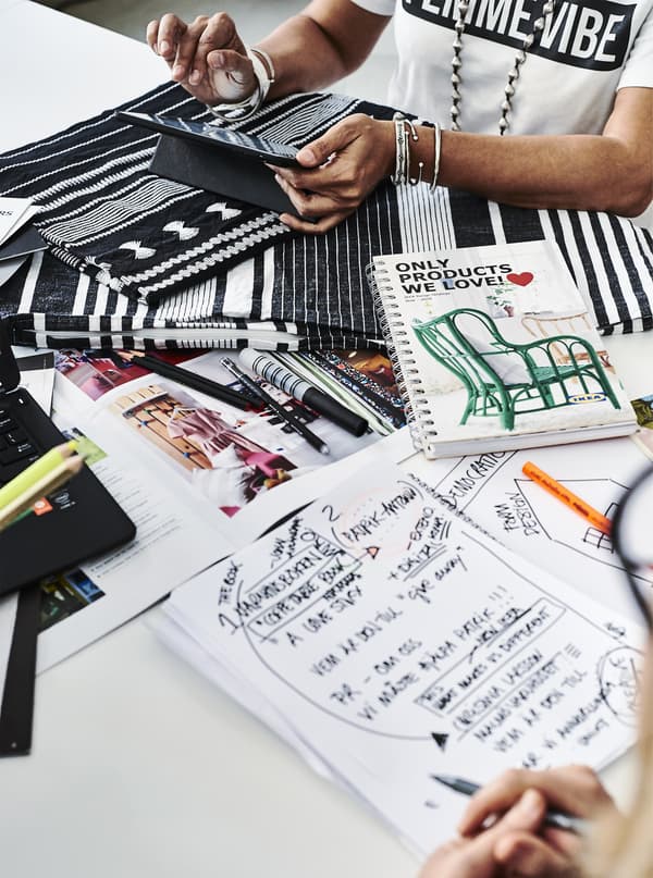 Two people working with fabric and notepads at a desk.