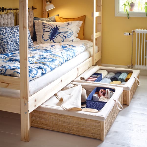 Two rattan IKEA RÖMSKOG bed storage boxes, pulled out from under the bottom of a bunk bed, containing clothes.