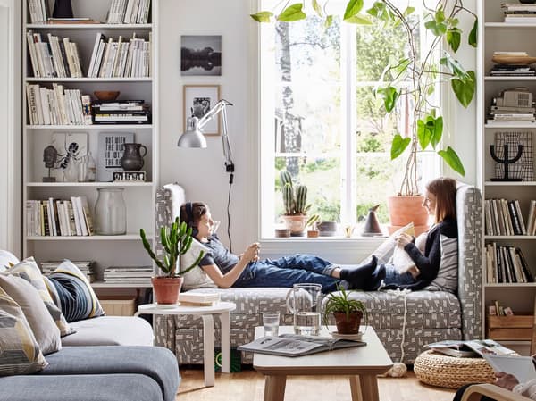 Two sisters sitting in modular sofa units, facing each other in between a pair of white bookcases.