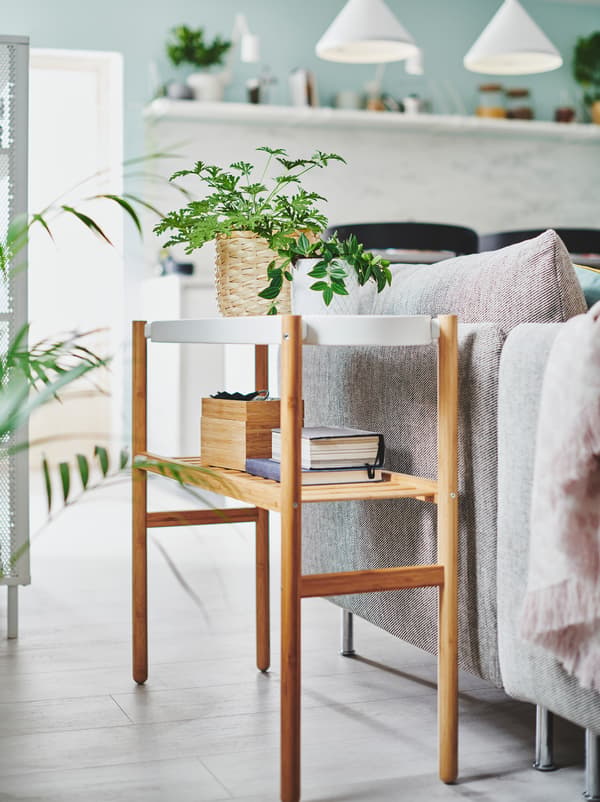 Two small, potted plants along with very light storage on a SATSUMAS plant stand placed next to a living-room sofa.