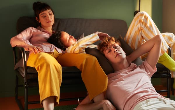 Two students chilling in a sofa bed while another student relaxes on the floor in a dorm room.