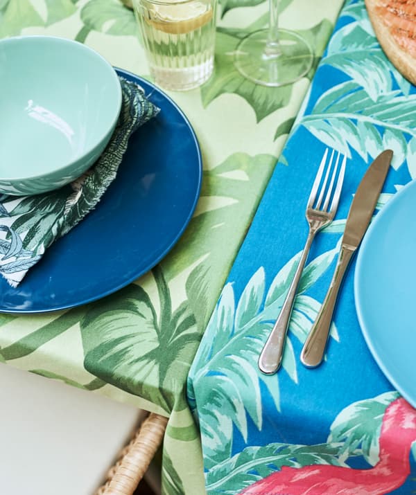 Two tables pushed together, one covered in a green leaf tablecloth, one with blue patterned fabric, each set with plates.