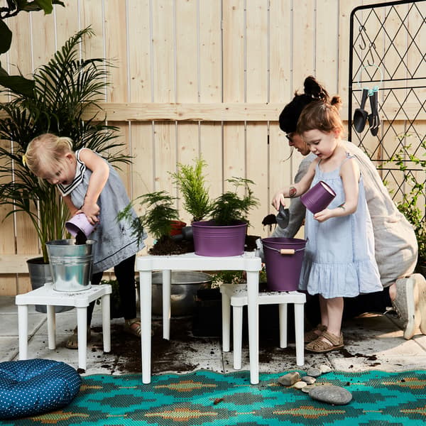 Two toddlers and a parent putting dirt into plant pots