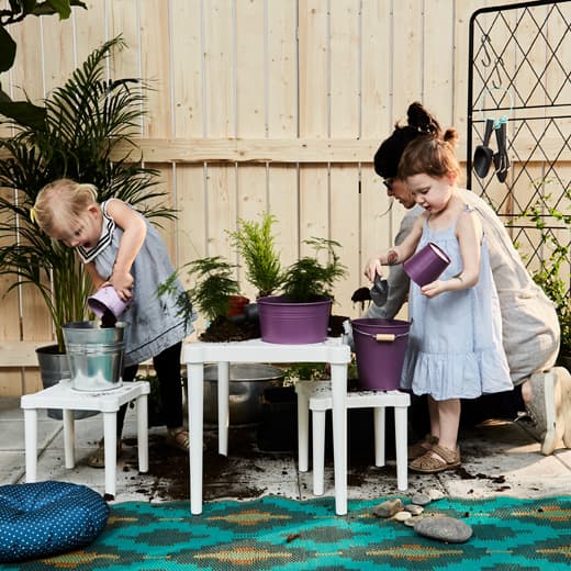 Two toddlers and a parent putting dirt into plant pots