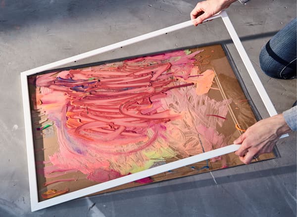 Two toddlers squeezing paint onto brushes and playing with chalk and a close-up showing the child’s art being placed into a plastic frame