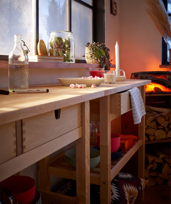 Two wheeled kitchen trolleys placed along a wall, forming a long side table; plate of after-dinner sweets and candle on it.