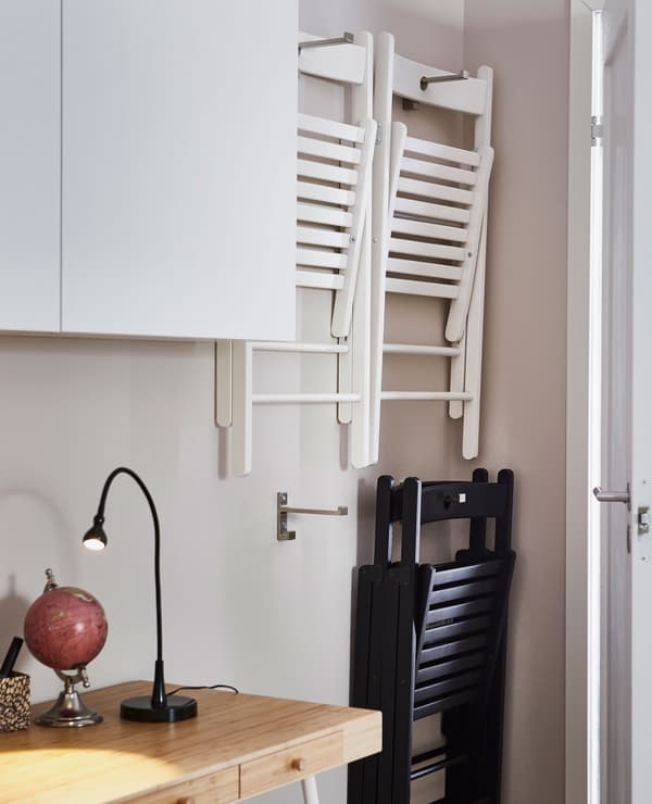 Two white fold-up chairs hanging on the wall on mounted BJÄRNUM stainless steel hooks behind a living room door.