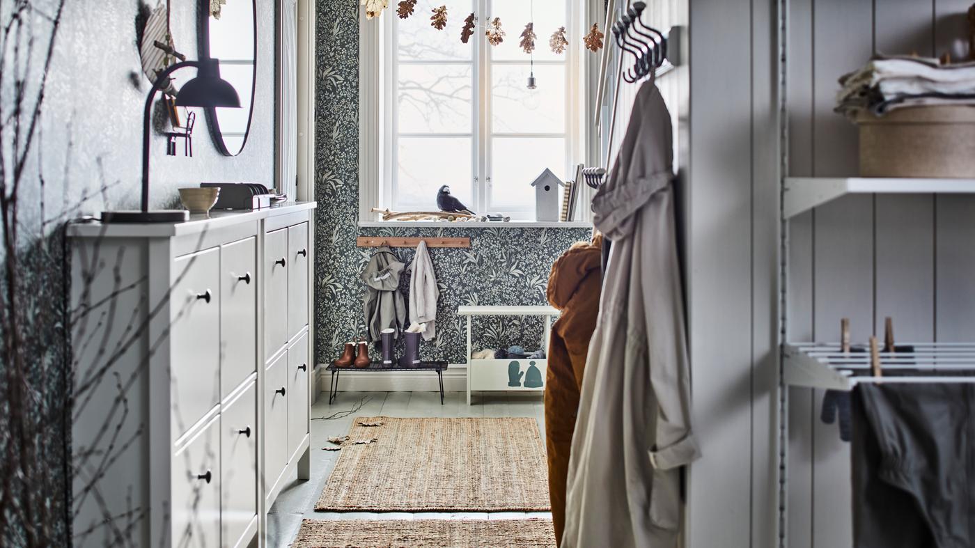 Two white HEMNES shoe cabinets with 4 compartments are in a bright hallway opposite some clothes hanging from hooks.
