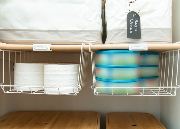 Two white OBSERVATÖR clip-on baskets attached to a shelf, filled with toilet paper and baby necessities.