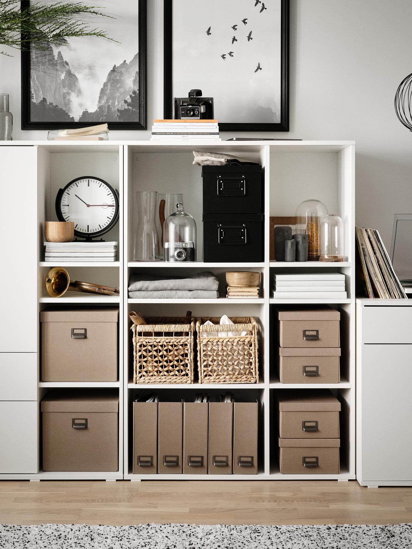 Two white VIHALS open shelving units side by side filled with storage boxes, baskets and other objects including a clock.