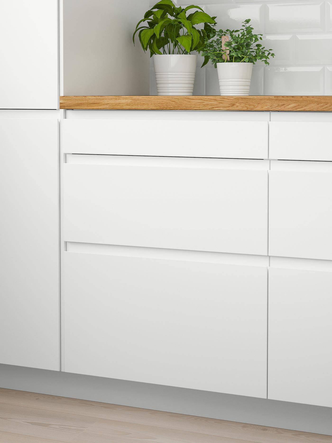 Two white wall cabinets with doors and a wooden worktop with two green plants on top and six white drawers below.