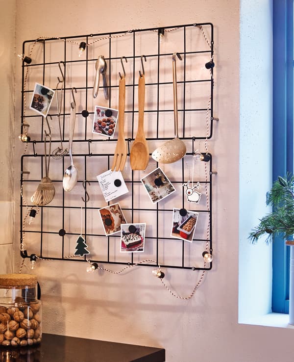 Two wire trellises hang on a kitchen wall, displaying cooking utensils, recipes and decorations.