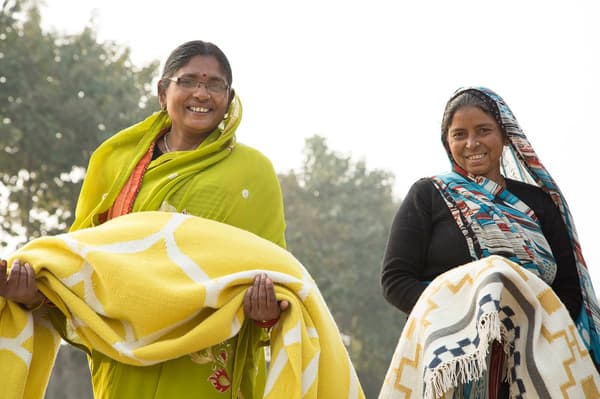 Two women holding hand-woven IKEA rugs.