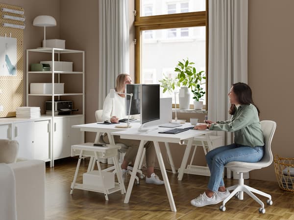 Two women in a workspace at home with two white TROTTEN desks, two LÅNGFJÄLL office chairs and computer screens.
