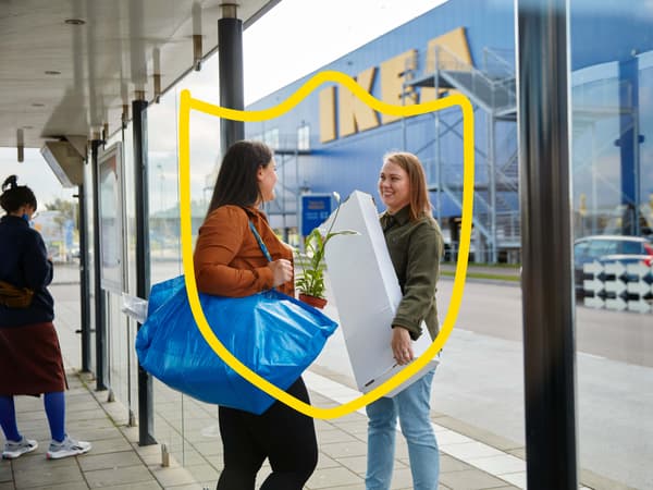 Two women talking outside an IKEA store, one holding a blue FRAKTA bag and the other a white box.
