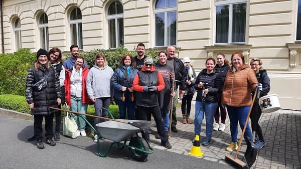 Tým dobrovolníků uklízí venkovní prostranství před budovou. Skupinová práce, úklid zeleně, komunitní akce, zahrada, kolektiv.