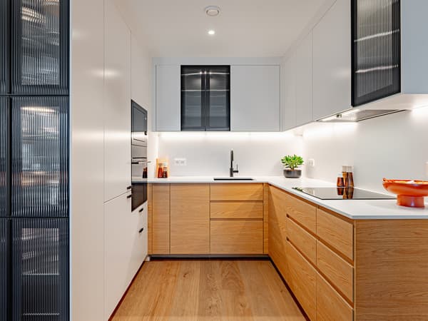 U‑shaped kitchen with white cabinets, oak veneer drawer fronts, a light countertop, and anthracite reeded glass cabinet doors, featuring integrated appliances and under‑cabinet lighting.