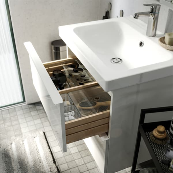 Un baño blanco con gris muestra un cajón abierto con cajas dentro que ayudan a organizar tu baño.