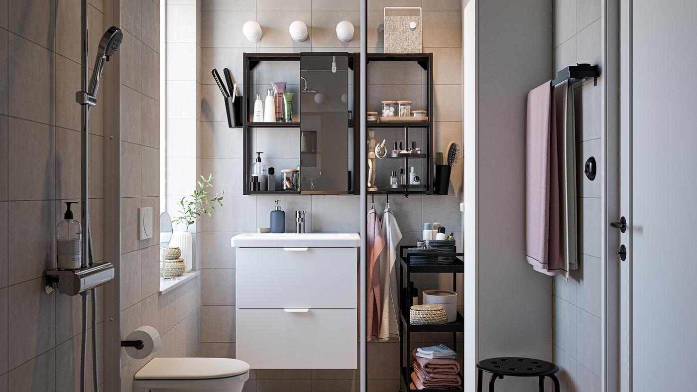 Un baño con muebles de baño en blanco y negro, un set de ducha cromado, toallas de color rosa claro y una ducha en vidrio.