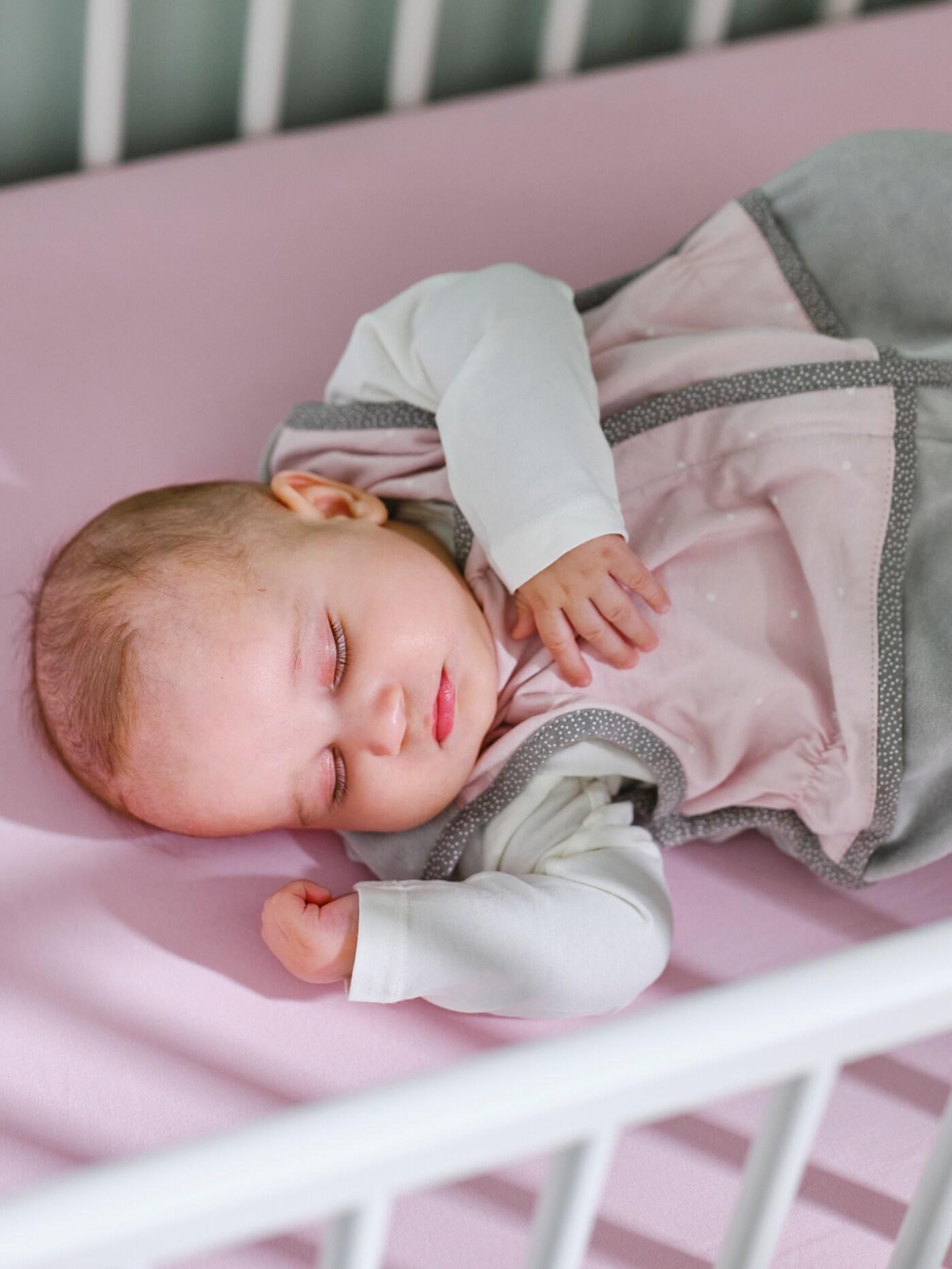 Un bébé dans une gigoteuse LEN rose sur un drap housse LEN rose dort dans un lit bébé GULLIVER blanc.
