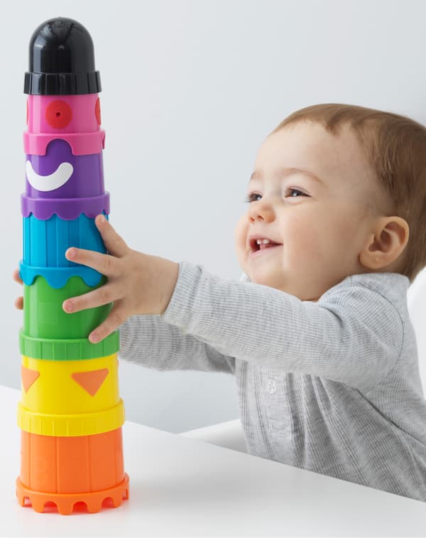 Un bimbo seduto su un seggiolone si aggrappa a una torre di costruzioni MULA fatta di bicchieri colorati, costruita su un tavolo - IKEA