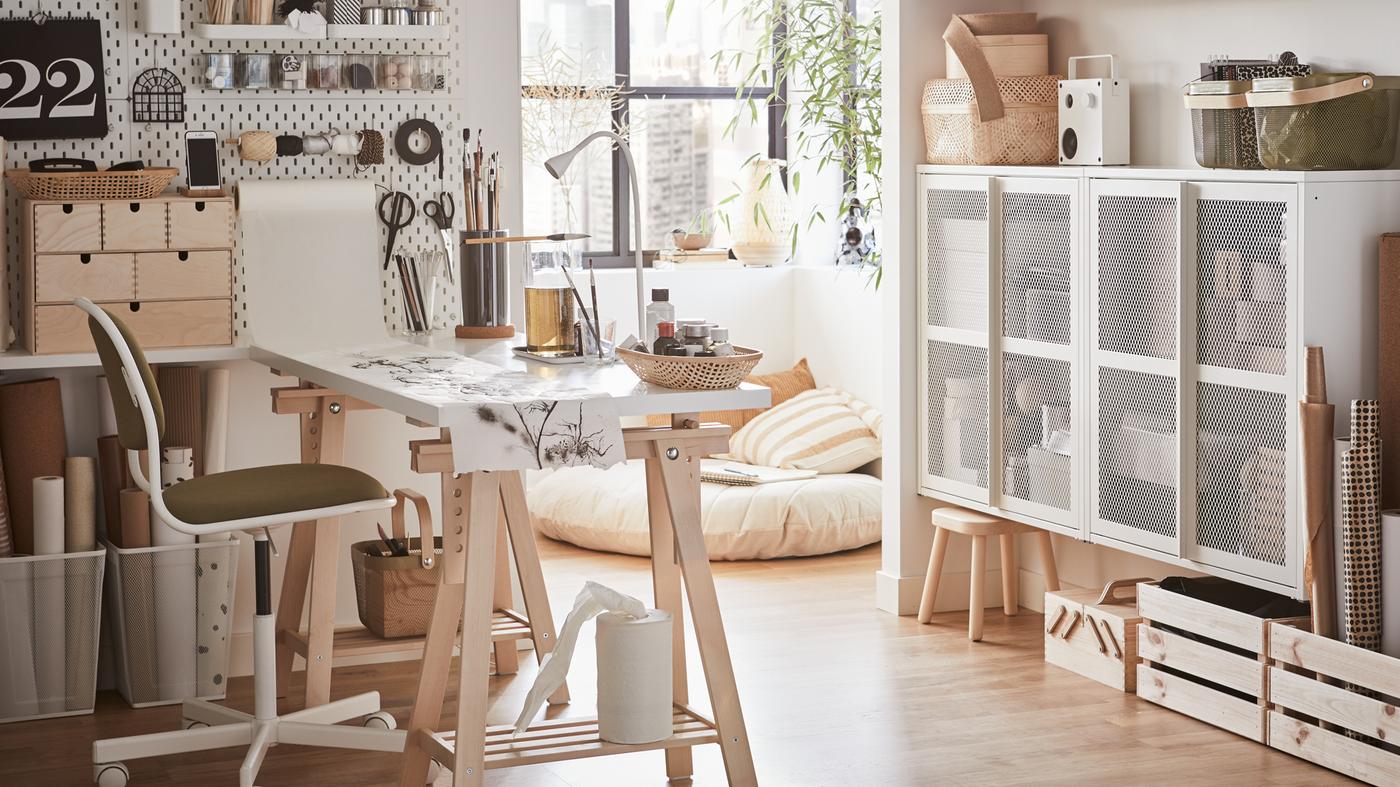 Un bureau à domicile lumineux avec un bureau blanc, une chaise pivotante blanc/jaune vert et un panneau perforé blanc avec du matériel de bricolage.