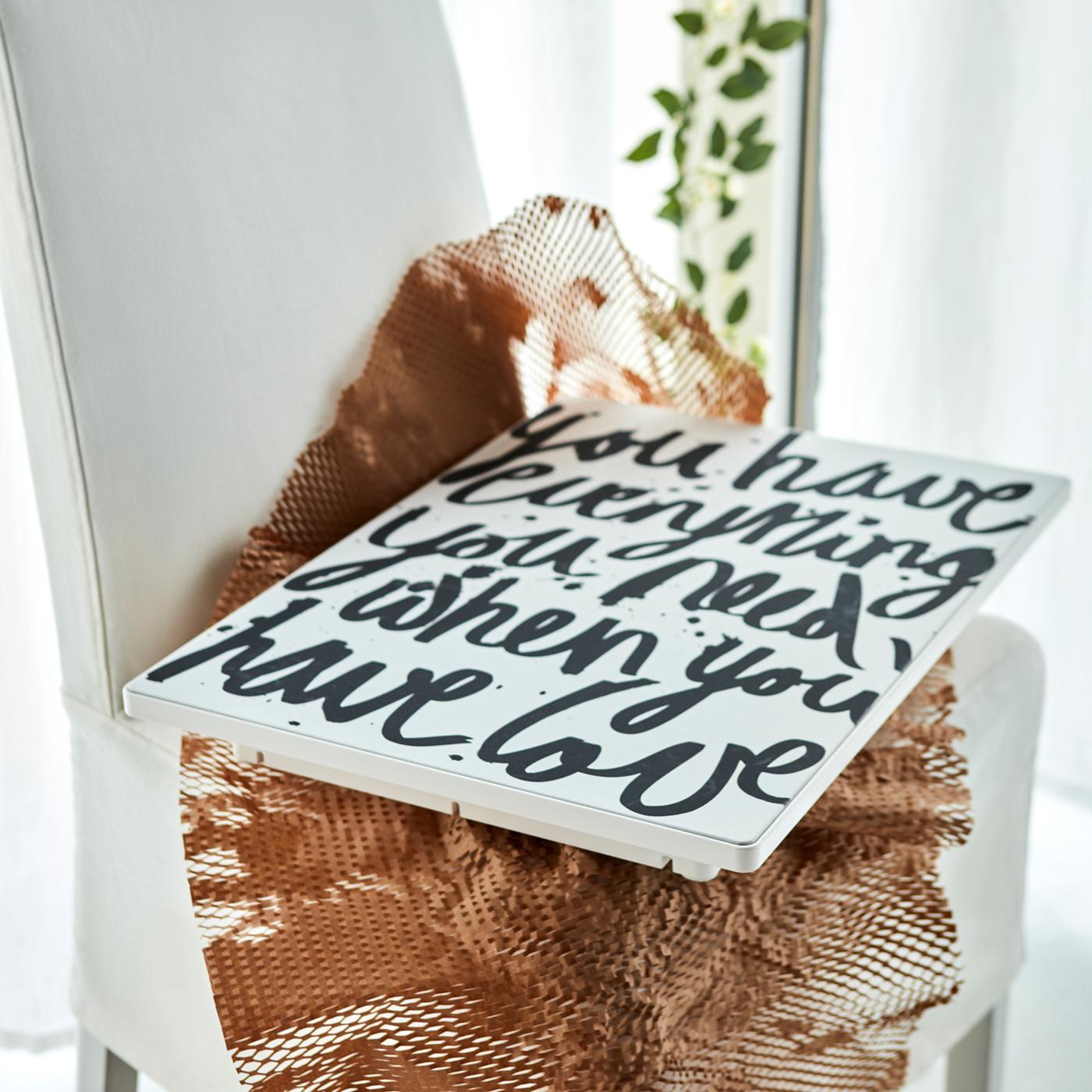 Un cadre avec haut-parleur Wi-Fi SYMFONISK avec un message d’amour en image sur du filet placé sur une chaise en tissu.