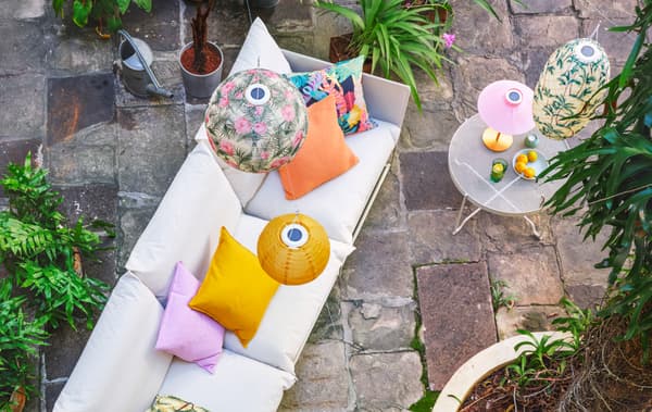 Un canapé blanc dans un patio en pierres naturelles. Les coussins sur le canapé et les suspensions au-dessus sont de couleurs vives et à motifs colorés.