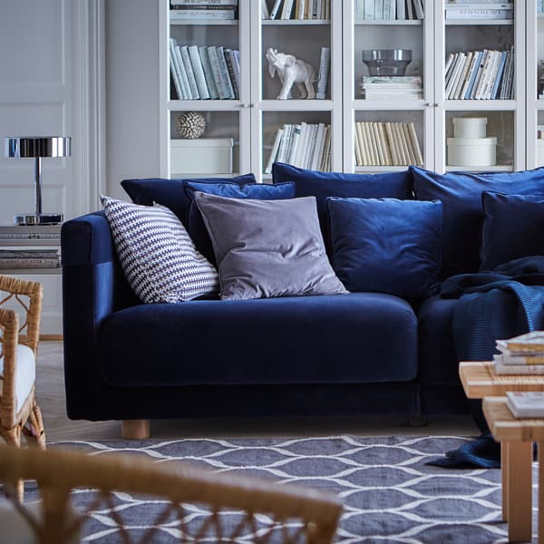 Un canapé bleu foncé en velours STOCKHOLM 2017 rempli de coussins et posé sur un tapis bleu à motif dans une salle de séjour.