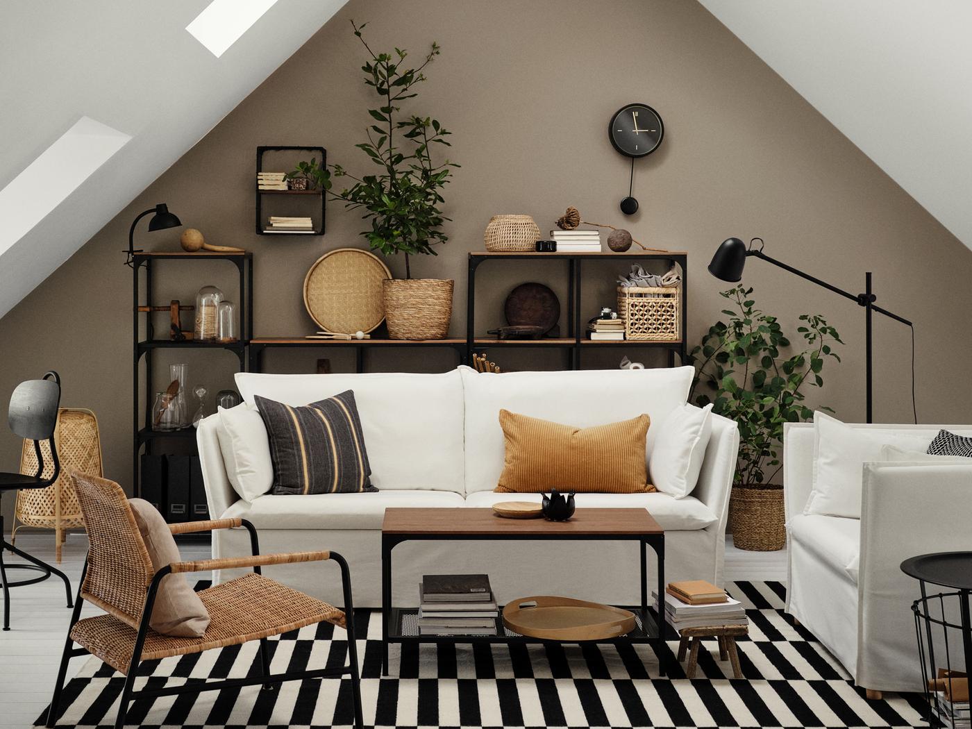 Un canapé trois places BACKSÄLEN blanc et des fauteuils sont disposés autour d’une table basse, dans une pièce mansardée et aérée.