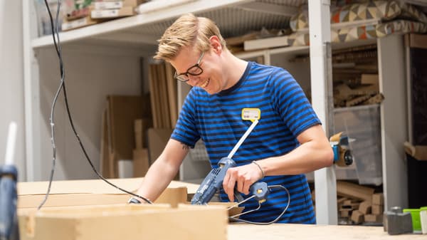 Un colaborador de IKEA vestido con ropa de ikea AREGLANDO UN MUEBLE DE MADERA.