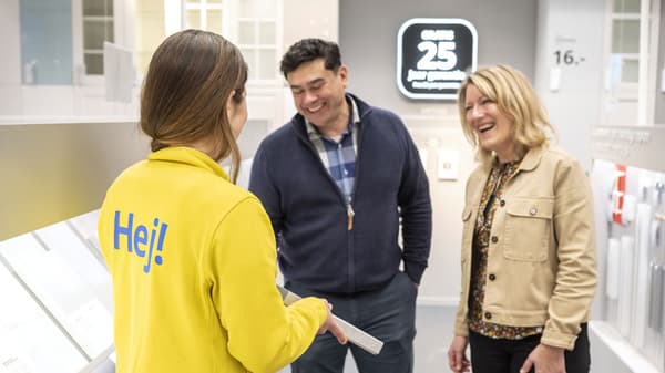 Un couple se trouve dans la section cuisine de IKEA et un collaborateur tient un échantillon de matériau d’armoire