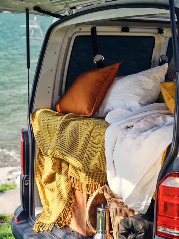 Un coussin orange et blanc cassé posé sur plusieurs couvertures à l'arrière d'une camionnette.