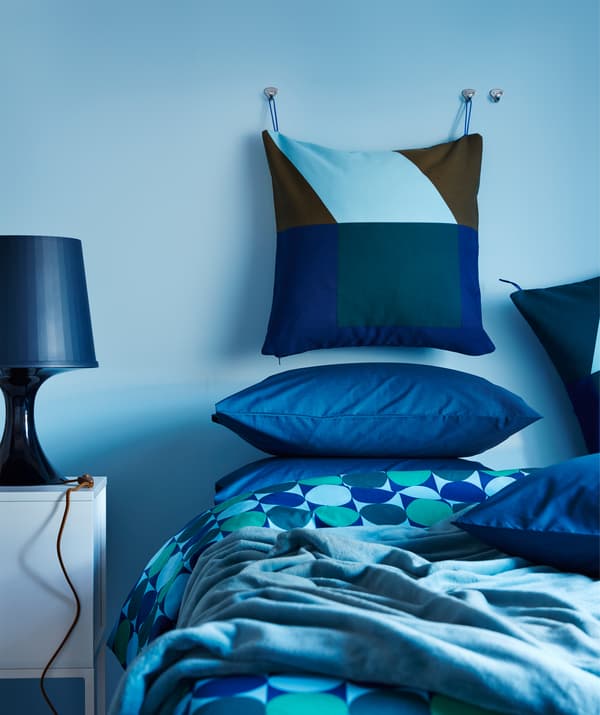 Un coussin revêtu d’une housse IKEA MAJALISA bleu et vert accroché au mur d’une chambre à coucher avec des textiles bleus.