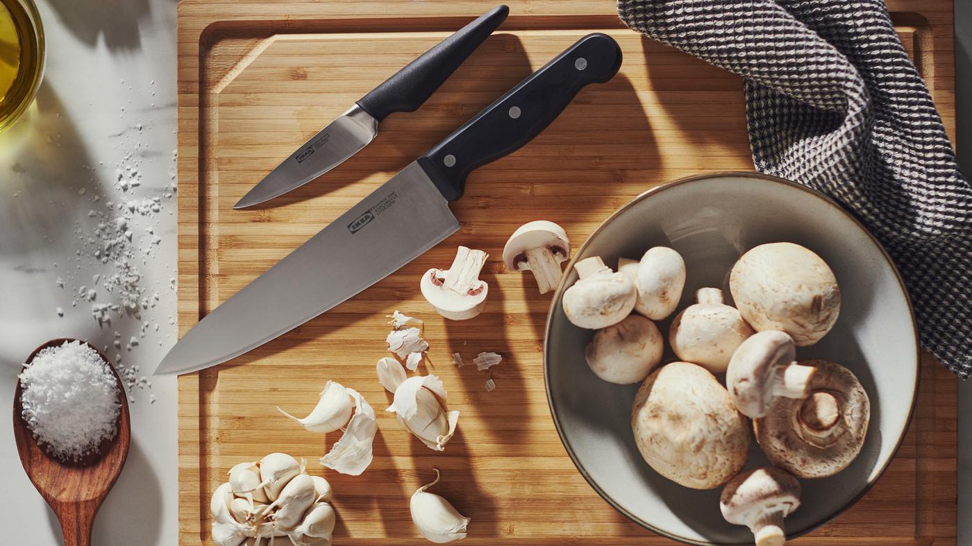 Un couteau de cuisine VARDAGEN, un couteau à éplucher VÖRDA, de l’ail sur un billot en bambou et un bol avec des champignons.
