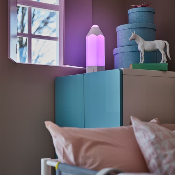  Un cuarto infantil con un clóset azul y una lámpara para mesa PELARBOJ que alumbra con una luz púrpura.