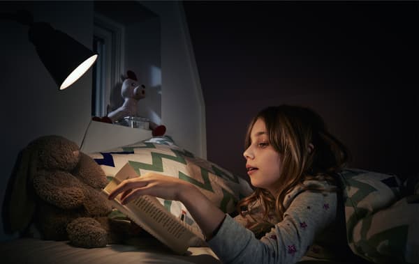 Un enfant lisant un livre au lit avec une lampe de lecture.