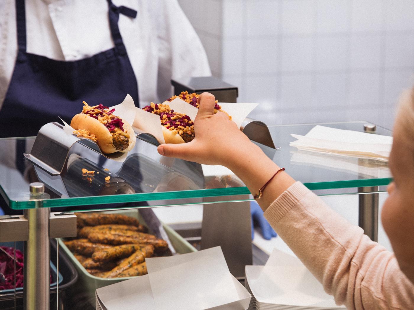 Un enfant portant un pull rose prend son hot-dog végétarien fraîchement préparé sur le comptoir d’un magasin IKEA.