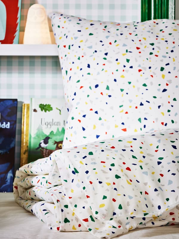Un ensemble de linge de lit MÖJLIGHET sur un lit non fait, avec une lampe à DEL SOLBO et des livres sur des cimaises sur un mur derrière.