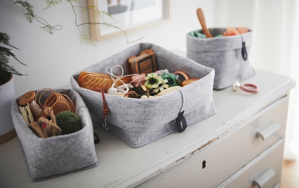 Un ensemble de paniers RAGGISAR en tissu remplis de babioles et de menus objets, posés sur une vieille commode usée.