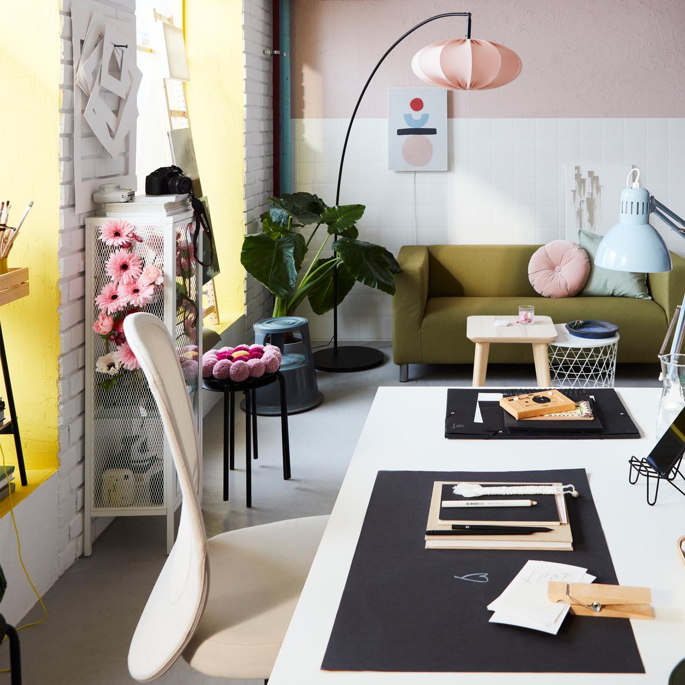 Un espace de travail avec un bureau TROTTEN, une chaise de bureau FLINTAN et des décorations roses. Un grand lampadaire incurvé se trouve derrière.