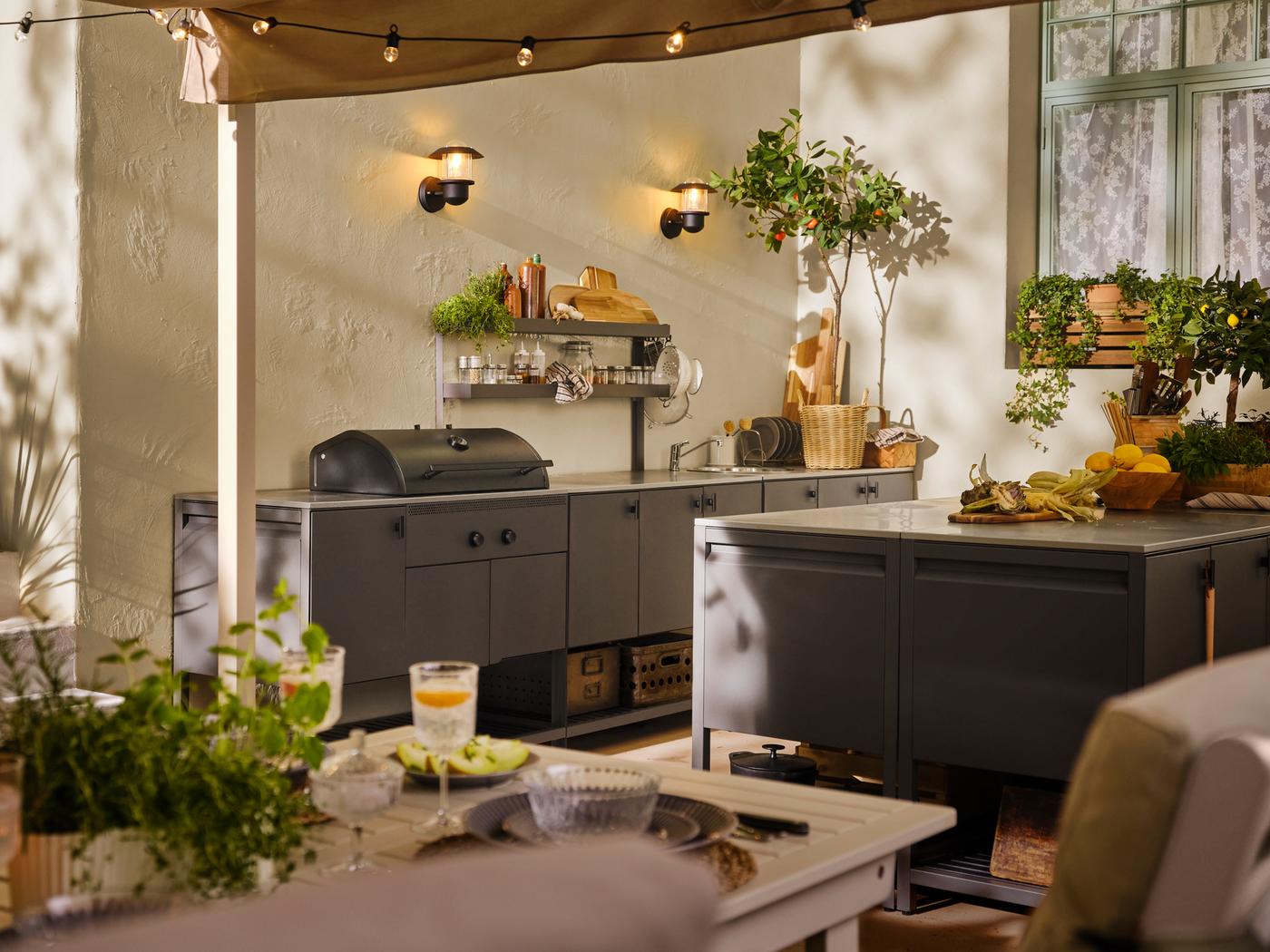 Un espacio exterior con una mesa BONDHOLMEN en blanco/beige, y varios módulos BÅTSKÄR en gris oscuro, incluido un asador de carbón.