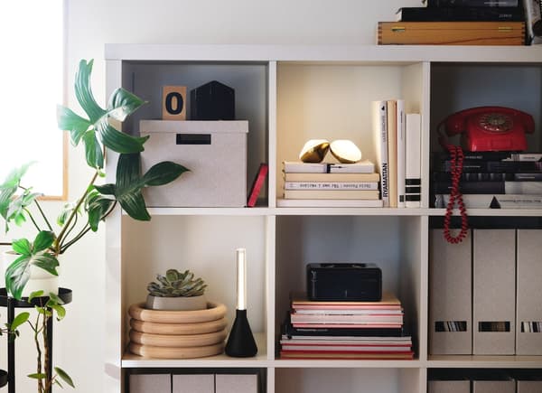 Un estante KALLAX blanco con decoraciones y libros en sus compartimientos.