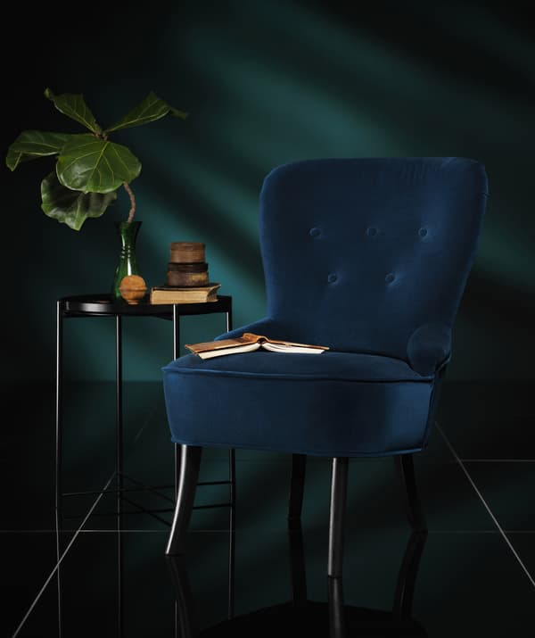 Un fauteuil en velours bleu foncé à côté d'une table basse dans une pièce sombre.