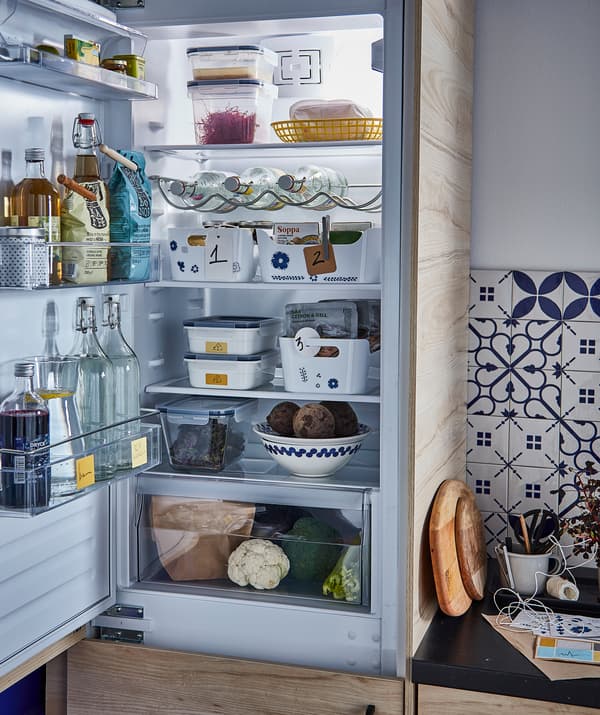 Un frigo ouvert avec de la nourriture et des boissons: des bouteilles dans la porte, des récipients sur les étagères, un tiroir à légumes en bas.