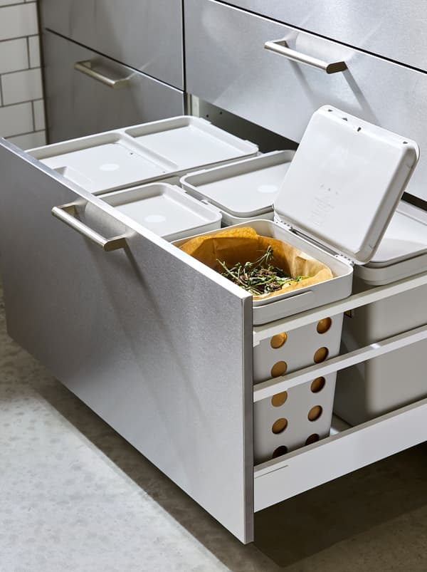 Un grand tiroir de cuisine ouvert avec une solution de tri des déchets HÅLLBAR, un couvercle soulevé révélant des déchets alimentaires.