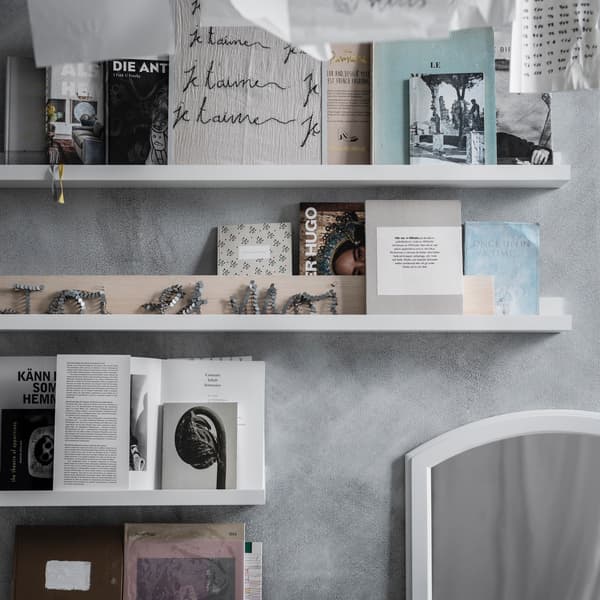 Un gros plan d’un mur gris avec des étagères murales blanches contenant des livres, des papiers et des images décoratives.