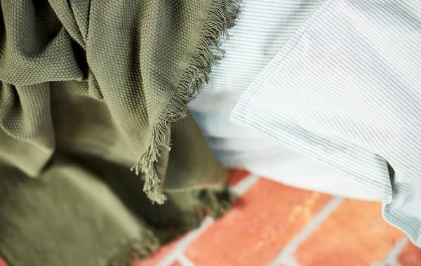 Un gros plan sur une couverture verte et un tissu rayé gris clair, avec un plancher en céramique rouge à l’arrière-plan.