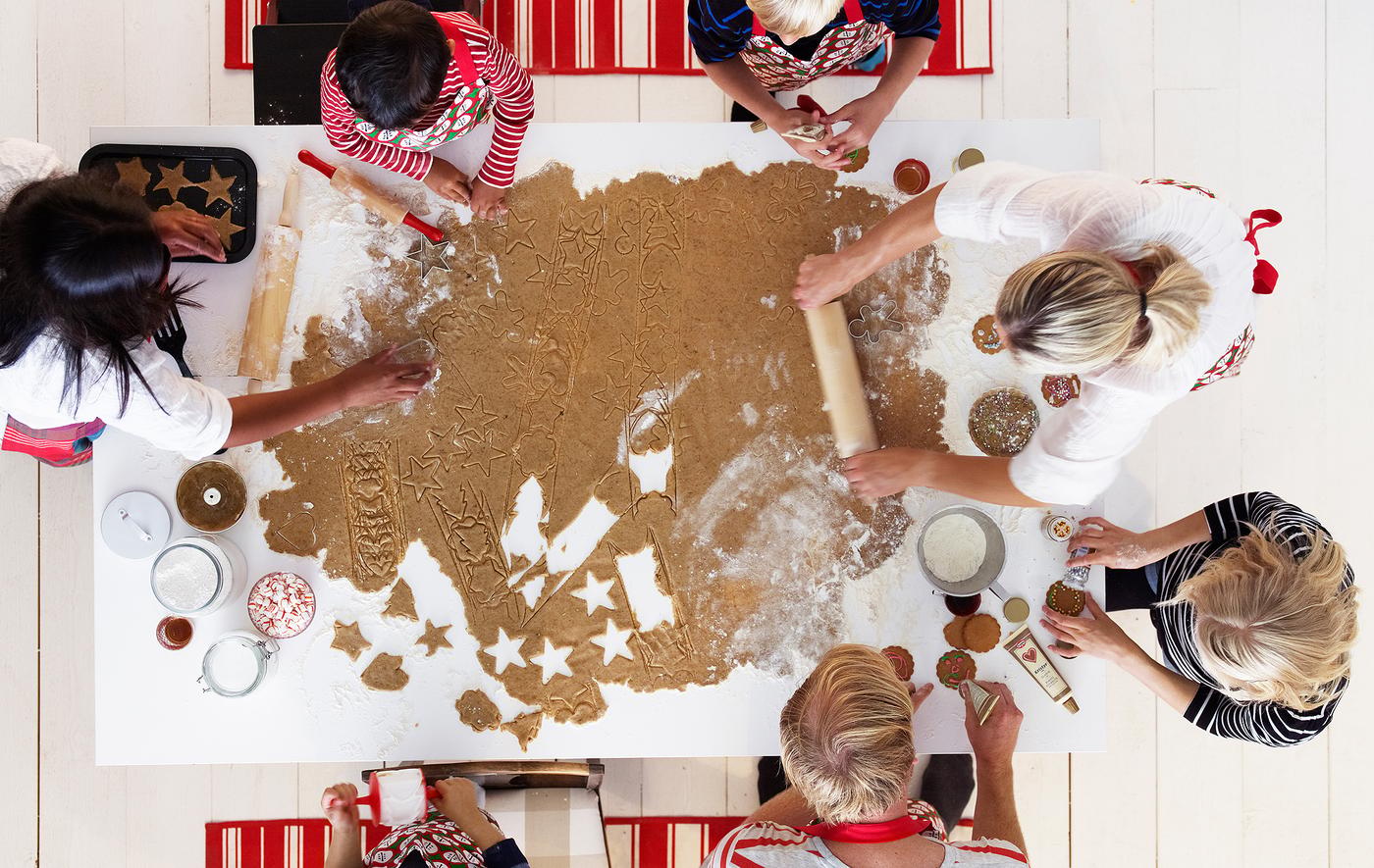 Un groupe d’adultes et d’enfants occupés à travailler une très grande pâte de biscuit à pain d’épices sur une table de cuisine.
