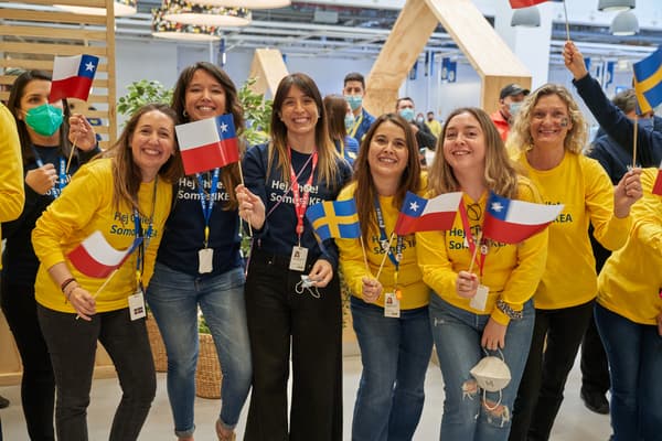 Un grupo de colaboradores de IKEA usando poleras amarillas y azules abrazados y sonriendo, sosteniendo banderas de Chile y Suecia.